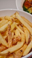 Close-up of golden fried potato sticks served in a white bowl with crispy texture and light seasoning. Concept of comfort food, casual dining and simple homemade snack
