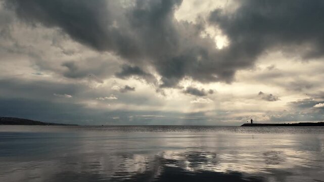 Dramatic Cloudy Sky Over Calm Sea with Distant Lighthouse, Water Surface Reflection of Dark Clouds and Sun Rays, Beautiful Tranquil Coastal Landscape at Golden Hour in B&uuml;y&uuml;k&ccedil;ekmece