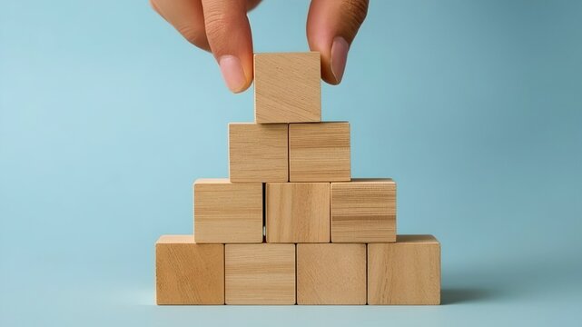 A hand meticulously arranging wooden blocks to create a pyramid