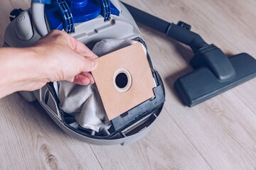 A Close-Up View of a Hand Inserting a Paper Dust Bag Inside a Vacuum Cleaner's Compartment on a Wooden Floor