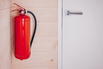 A Bright Red Fire Extinguisher Mounted on a Wooden Wall Beside a Modern Door for Efficient Fire Safety Preparedness