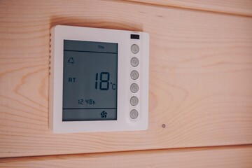Digital Temperature Control Displaying Current Room Temperature and Settings with a Minimalist Design on a Wooden Wall