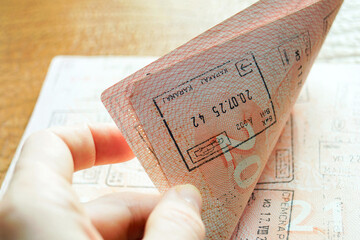 Close-up of fingers gripping a passport page showing entry stamps and markings. Represents active...