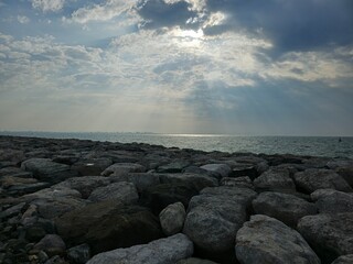 Sunset view from cloudy sky over the Sea with Rocks at beach. A beautiful sunset over the ocean with a large rock in the foreground. The sky is a mix of orange and pink hues, and the water is calm
