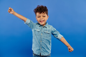 Joyful moment of a stylish curly-haired boy enjoying playful fun in a blue studio