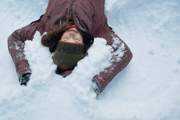 Mid adult woman enjoying of lying on snow in winter with closed eyes