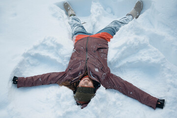 Happy woman enjoying winter and making snow angel.