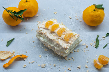 A delicious meringue roll with fruit. A top view of the meringue cake and tangerines against a gray background.