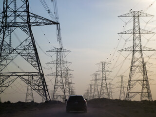 Car at Empty road upon Electricity tower with stormy sky in background and SUV driving down road Electric transmission tower pylons stretching across. AERIAL View of High voltage power line Background