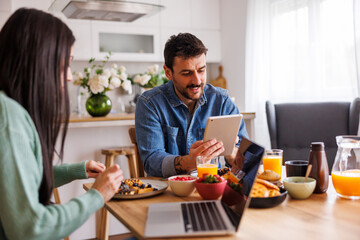 Couple using laptop and tablet computers while having breakfast at home