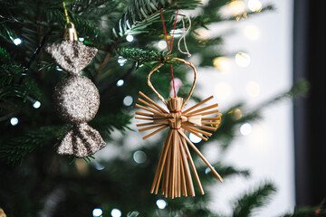 Straw angel and shiny candy Christmas ornaments on tree with soft focus, festive postcard flyer design and copy space