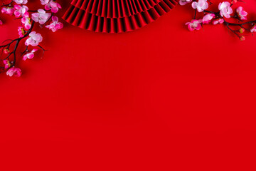 Bright vibrant gold and red Chinese New Year background with mandarin oranges, blossom tree branches, decorative fans, festive greeting envelops and coins, traditional Chinese New Year ornaments