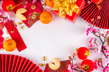 Bright vibrant gold and red Chinese New Year background with mandarin oranges, blossom tree branches, decorative fans, festive greeting envelops and coins, traditional Chinese New Year ornaments