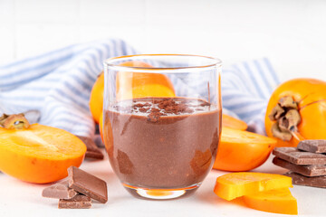 Sweet persimmon chocolate mousse, healthy vegan dessert with no added sugar, diet dessert food, with raw fresh persimmon fruit puree, chocolate or cocoa powder, on white kitchen table