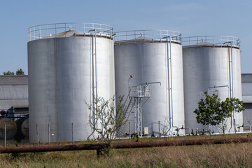 Three large tanks are sitting in a field. The tanks are silver and are next to a fence
