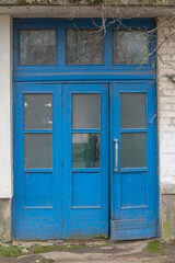 Weathered blue wooden double entrance doors with transom windows.