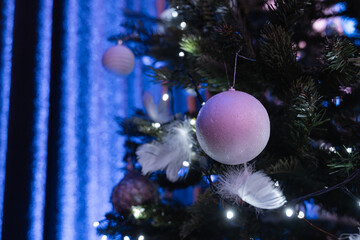 Close up of white christmas ball ornament with feathers and lights on decorated tree in elegant festive interior with blue bokeh background