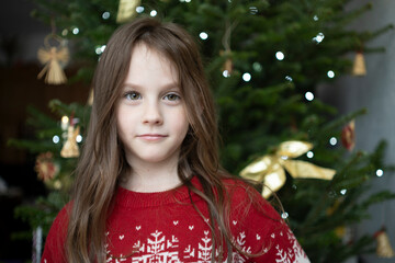 Close up of girl in red Christmas sweater near decorated tree, playful sideways gaze filled with warmth and festive emotion indoors