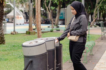 A young Indonesian Muslim woman throwing rubbish in a trash can in a city park