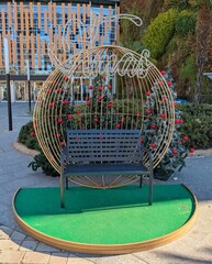 Banco de metal con &aacute;rboles de navidad decorados con bolas de navidad y palabra Xmas en ne&oacute;n en el exterior de un centro comercial 