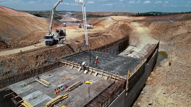 Aerial view of workers pouring concrete on a reinforced slab using a concrete pump at a highway construction site. Large-scale civil engineering and infrastructure development project.