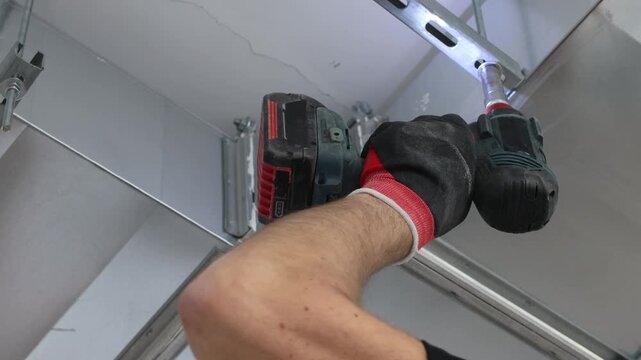 Close-up of construction worker installing metal ceiling frame using cordless drill. Professional drywall ceiling installation, interior renovation process, suspended ceiling system, building construc