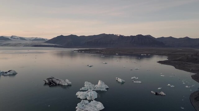 Golden hour aerial flight reflecting warm sunset light on blue ice chunks at J&ouml;kuls&aacute;rl&oacute;n lagoon, Iceland.