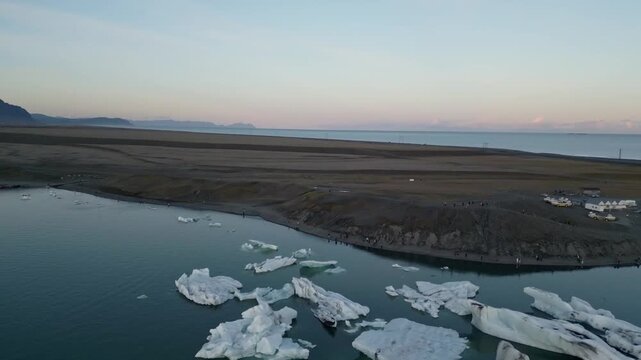 Golden hour aerial flight reflecting warm sunset light on blue ice chunks at J&ouml;kuls&aacute;rl&oacute;n lagoon, Iceland.