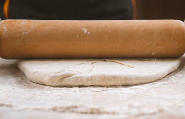 Chef is rolling the dough with the rolling pin on the on the table. Hands close-up.Cooking pasta, bread,spaghetti,khachapuri, food concept