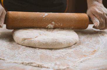Chef is rolling the dough with the rolling pin on the on the table. Hands close-up.Cooking pasta, bread,spaghetti,khachapuri, food concept