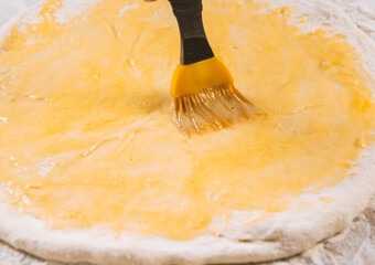 Pizza dough, chef spreading egg yolk with pastry brush in kitchen