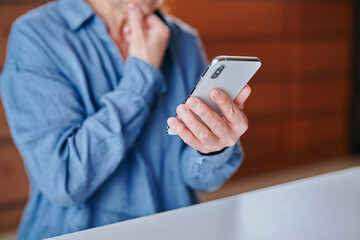 部屋でスマホを操作するシニア女性