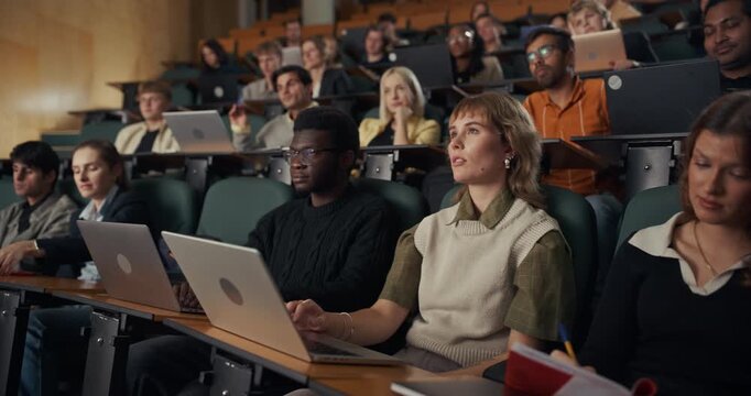 Diverse Group of University Students Sit in Lecture Hall, Concentrating on an Academic Presentation While Typing on Laptops, Writing Notes, Higher Education Class, Modern Learning and Study Skills.