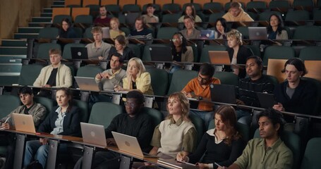 Diverse University Students Sit in Lecture Hall, Typing on Laptops, Jotting Notes, and Concentrating on an In-depth Higher Education Lesson, Research Concepts, and Collaborative Academic Learning.