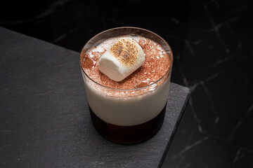 An overhead shot of a delicious marshmallow cocktail. A clear glass is placed on a stone surface 
