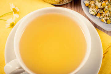 Chamomile tea with a cup in focus and dried chamomile in the background. Herbal infusion (Matricaria chamomilla) with soothing calming properties for wellness.