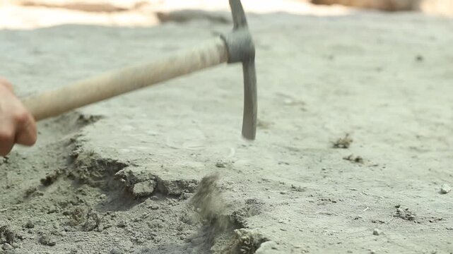 Close up view of a metal pickaxe striking dry sandy soil repeatedly. This footage depicts concepts of hard manual labor, agriculture, gardening, and construction site excavation work.

