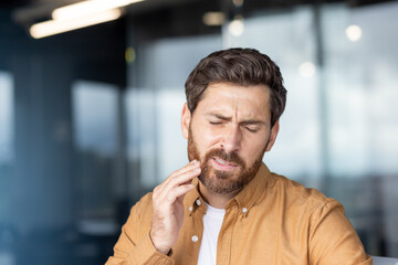Obraz premium Young man experiencing an acute toothache or dental pain, touching his jaw with a hand, depicting discomfort, dental problems, and the need for urgent dental care or treatment