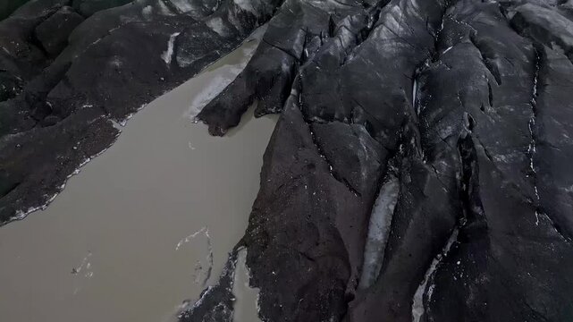 Cinematic aerial drone view of Sv&iacute;nafellsj&ouml;kull glacier tongue showing dramatic blue ice and volcanic ash textures in Iceland 4K.