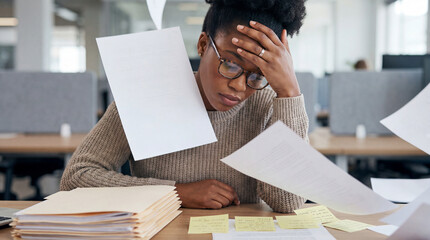Overwhelmed young professional struggling with workplace stress while managing paperwork overload in a busy modern open plan office