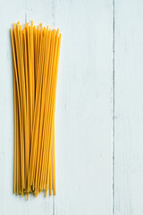 A neat bunch of dry, uncooked spaghetti lies vertically on a white, rough wooden background, leaving plenty of room for text on the right.