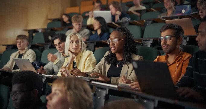 University Students Sit in Lecture Hall, Typing on Laptops, Exchanging Ideas, and Taking Detailed Notes While Listening to an Academic Presentation, Collaborative Study, Active Participation