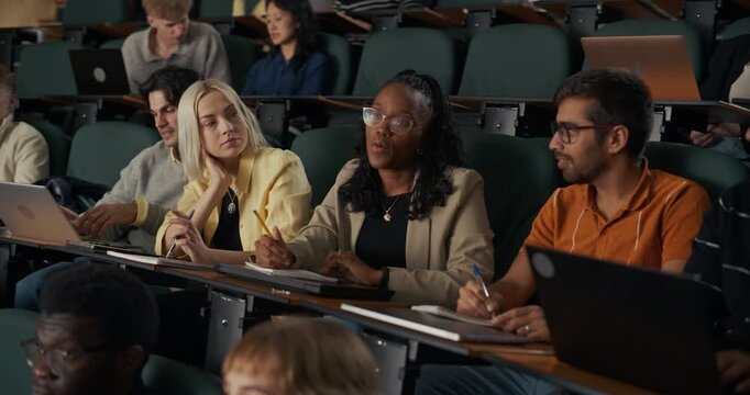 University Students Sit in Lecture Hall, Listening, Raising Hands to Ask Questions, They Engage With an In‑depth Academic Presentation on  Learning, Critical Thinking, Course Participation.