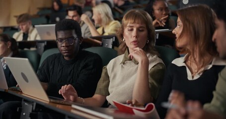 College Classmates Sit Together in a Crowded Lecture Hall, Using Laptops and Notebooks, Solve Problems, and Discuss Course Material While Following an University Lesson on Collaborative Study