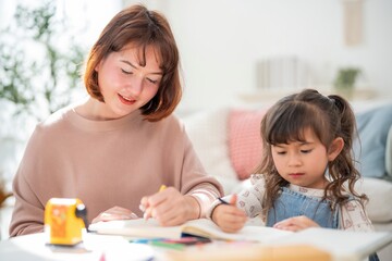 Mother and daughter engage in drawing and writing activity indoors during daylight hours in a cozy home setting