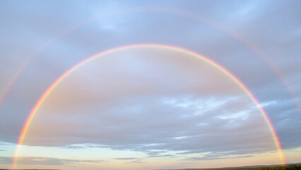 Obraz premium Vibrant Rainbow Arching Across a Cloudy Sky After a Rain Shower.