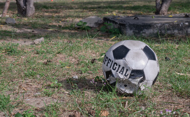 A black and white soccer ball, which is old and damaged, is resting on a patch of grass in the park.