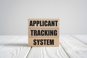 Minimalist image of three stacked wooden blocks displaying APPLICANT, TRACKING, and SYSTEM in bold black text on a light wooden surface, evoking a modern, professional atmosphere.