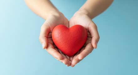 Obraz premium Hands gently holding a red heart symbol against a light blue background representing love, care, compassion and emotional support