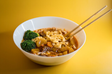 Vegetable noodle soup with broccoli in white bowl on yellow background